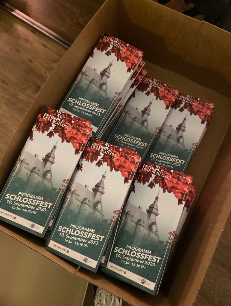 Ein Karton voller gedruckter Programmflyer zum Schlossfest mit dem roten Ahorn-Motiv und dem Schlossturm