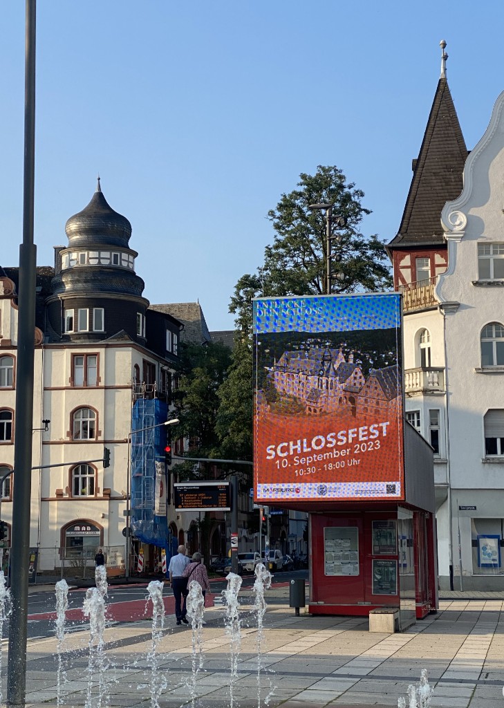Digitale Werbestele am Rudolphsplatz in Marburg zeigt das Schlossfest-Motiv mit Luftaufnahme des Schlosses